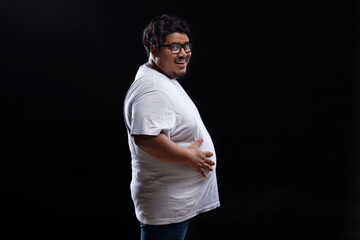 Portrait of a fat man smiling while placing hands on belly against plain background.
