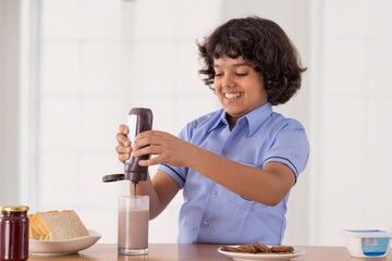 Young boy in school uniform pouring chocolate syrup into a glass of milk - Powered by Adobe