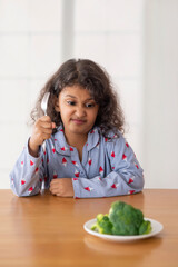 A Girl sitting in front of a plate of broccoli with a disgusted look on her face