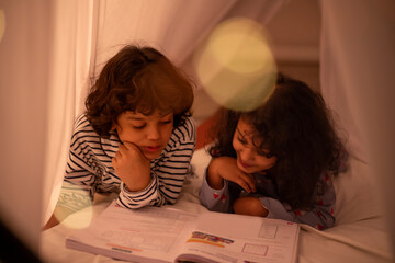 Sibling studying book together on bed attentively