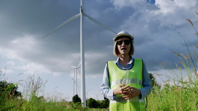 Asian female engineer or reporter is explaining or reporting the specification of wind turbines in wind farms, clean energy concept, renewable energy, save the world.
