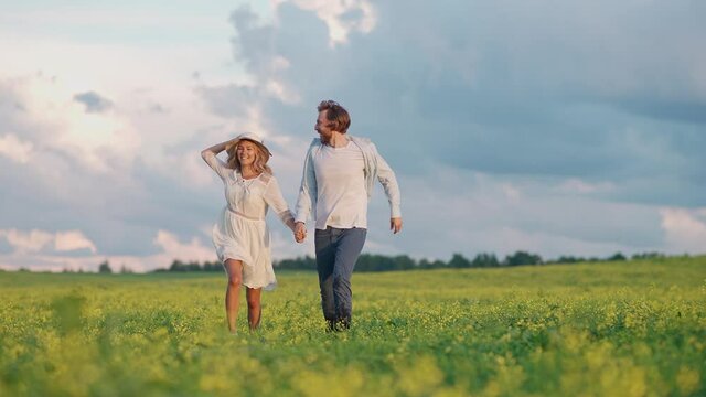 Countryside, cheerful young couple in nature, man and a woman are running through a field of rapeseed holding hands, slow motion.