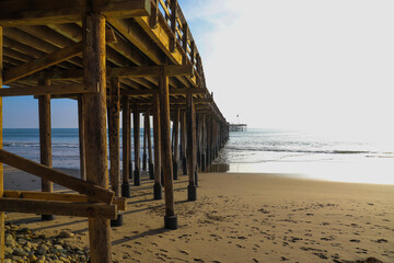 a shot of a long winding brown wooden pier at the beach with silky brown sand and vast blue ocean...
