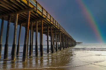 a shot of a long winding brown wooden pier at the beach with vast blue ocean water rolling and a...