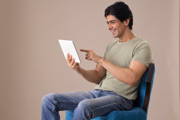 Happy Indian man watching tablet while sitting on chair