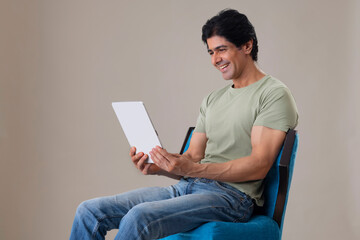 Happy Indian man watching tablet while sitting on chair