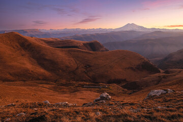 Autumn mountains at sunset. Mount Elbrus in the background. In front of the valley with fog.