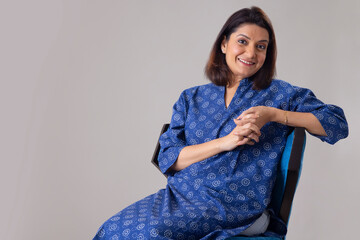 Happy Indian woman posing in front of camera while sitting on chair