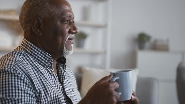 Tracking shot portrait of peaceful senior african american man resting with cup of coffee at home interior, free space