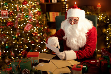 Fototapeta na wymiar Santa Clause is prepares gifts for children for Xmas at his desk while reading wish lists at home 