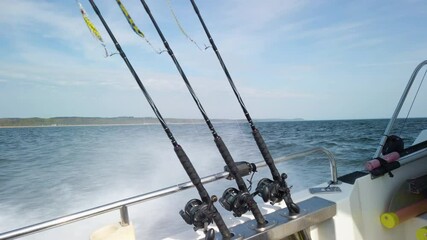 Three fishing rods hooked up with spinners, ready for fishing. The rods are lined up in a row on a small fishing boat. It is a beautiful sunny spring day.