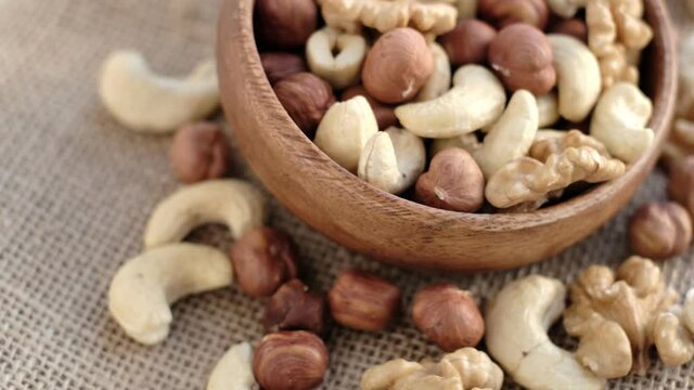 mixed nuts in a wooden cup against the background of fabric from burlap. Walnut, hazelnuts and cashews. Wood bowl with different tasty nuts