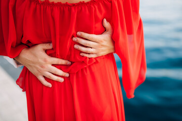 Man's hands hug a woman in a red dress around the waist. Close-up
