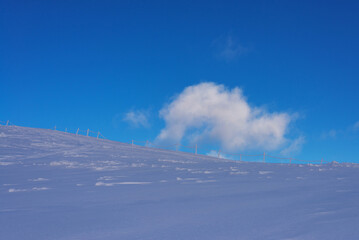 The snow-covered slope of the mountain under the blue sky. Restrictive columns on the snow-covered slope of the mountain.