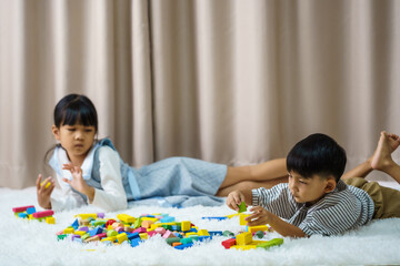 Children play with colorful toy blocks. Little boy and girl is building a tower of toy blocks sitting on a dark floor in a bright livingroom.