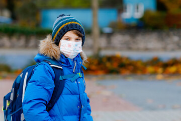 Little kid boy wearing medical mask on the way to school. Child backpack satchel. Schoolkid on cold autumn or winter day with warm clothes. Lockdown and quarantine time during corona pandemic disease