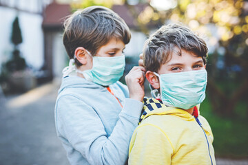Fototapeta premium Two kids boys in medical mask as protection against pandemic coronavirus disease. Children, lovely siblings and best friends using protective equipment as fight against covid 19.