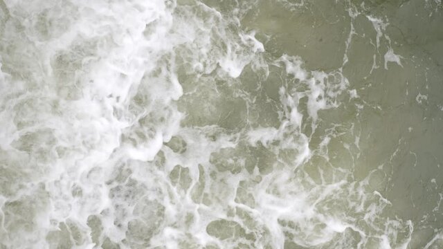 Top view of the sea waves that beat against rocks on cloudy day. Vertical video and slow motion