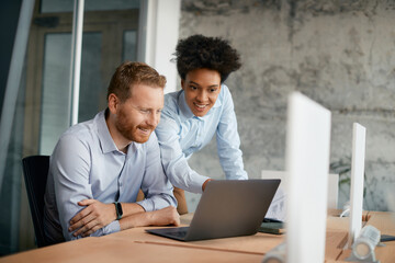 Happy business colleagues cooperate while using laptop and work in office.