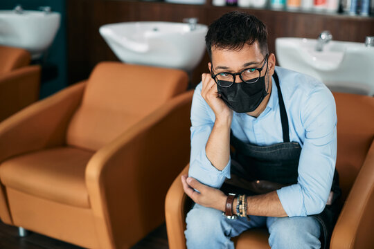 Distraught Hairdresser With Face Mask Sits At Empty Salon During Coronavirus Pandemic.