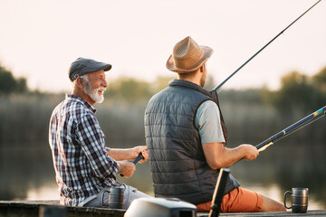 Happy senior man enjoys in freshwater fishing with his son in nature.
