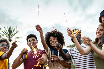 Group of united multiracial friends laughing and celebrating with sparkles outdoors - Young hipster...