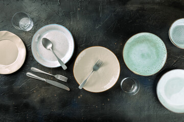 Obraz na płótnie Canvas Modern tableware set with cutlery and glasses, overhead flat lay shot on a black slate background. Elegant dinnerware