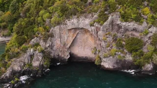 Maori artwork carved in rocky cliff on Lake Taupo coast. New Zealand popular tourist attraction - aerial orbit