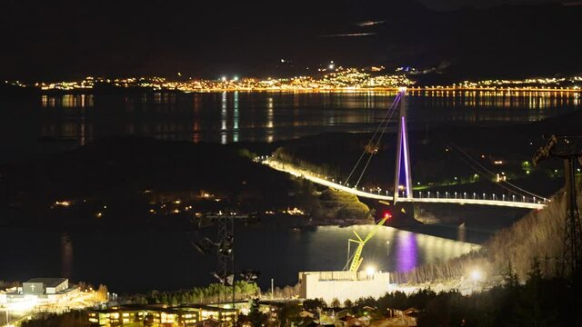 The H&aring;logaland Bridge near Narvik, Norway. The brightly lit suspension bridge spanning above the dark water of the fjord. Night city with busy traffic in the background.