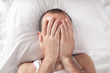 Caucasian depressed man lying in his bed and covering face.