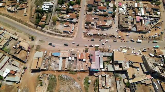 Aerial of traffic driving over road near slum town in rural Kenya