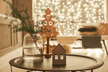 Decorated table in the Christmas interior. Christmas tree. Close-up a small house, Cones, garland, and other Christmas tree toys. light from the garlands