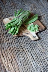 package of green flat beans tied with string on a cutting board. selective focus. front space blurred for copy, text space. vertical photograph. very old and rustic wooden base.