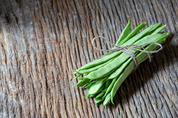 bunch of green flat beans tied with a string on an old wooden plank. sective approach. copy space, text space. horizontal photography.