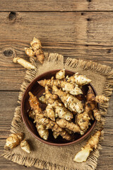 Raw Jerusalem artichoke in a bowl on wooden boards background