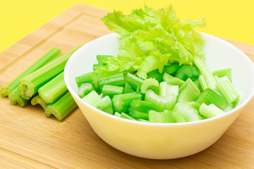 Fresh Chopped Celery Slices in White Bowl with Celery Sticks on Bamboo Cutting Board. Vegan and Vegetarian Culture. Raw Food. Healthy Diet with Negative Calorie Content