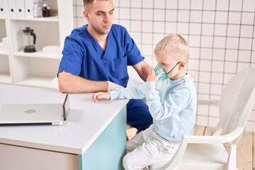 Obraz premium A pediatrician diagnoses lung disease and provides treatment. Breathe the medicine through a nebulizer inhaler.. Portrait of adorable little boy visiting doctor.