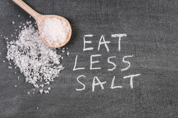 Wooden spoon on a chalk board. Eat Less Salt