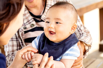 おばあちゃんに抱っこされた赤ちゃんがお母さんと戯れています　3世代が外のベンチに座っています