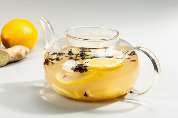 Hot ginger tea with lemon and honey in a glass cup on light grey background