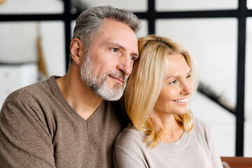 Middle-aged spouses sits on the sofa at home and look aside at one way. Close-up portrait of...