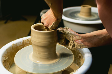 The woman potter's hands formed by a clay pot on a potter's wheel. The potter works in a workshop