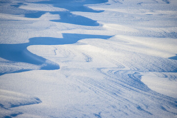 Fototapeta na wymiar Snow texture. Wind sculpted patterns on snow surface. Wind in the tundra and in the mountains on the surface of the snow sculpts patterns and ridges (sastrugi). Arctic, Polar region. Winter background