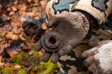 Man hands keep old iron fragments, clean them from dirt, clay, land and rust, after searching and producing scrap metal in forest.