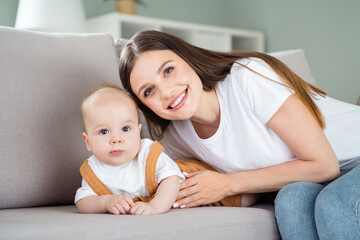 Portrait of attractive cheerful girl nursing watching baby on divan developing at home flat apartment indoors