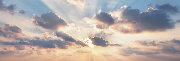 Beautiful fluffy clouds and rays of sunshine painted in dramatic colors at sunset