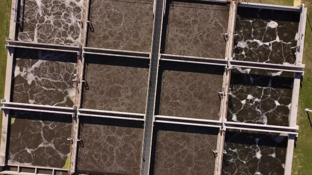 Ascending top down view of AySa water purification plant in Buenos Aires, Argentina containing square pools of dirty water before purification.