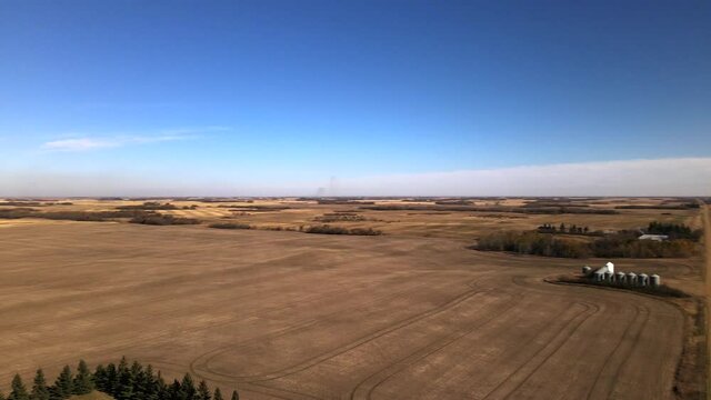 Fast aerial panning movement over vast and dry countryside landscape in Alberta's prairie. Sunny day over large farmland and straight dirt roads. Drone footage in 4k of rural tourism concepts.