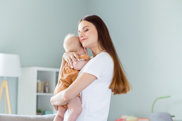 Profile side view portrait of attractive careful dreamy girl holding nursing embracing baby at light home flat indoors