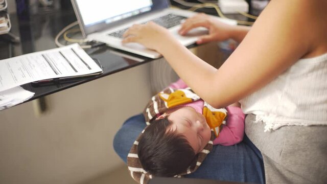 Baby Care Concept. Hispanic Newborn Baby Girl Sleeping On Her Mother's Legs Working At Home.